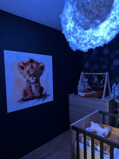 Tableau d’un lionceau attendrissant accroché dans une chambre de bébé au mur bleu foncé, éclairé par une lumière douce avec une suspension nuage lumineuse.