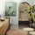 Wood-framed meditating frog illustration displayed in a natural, minimalist bathroom — bathroom wall art near an arched shower with plants, wood and rattan decor