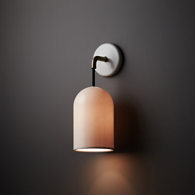 Applique murale suspendue au design minimaliste, avec un abat-jour cylindrique rose poudré et une fixation murale blanche et laiton. Idéale pour un éclairage doux et ciblé, parfait au-dessus d’un tableau ou en éclairage d’ambiance dans une déco chic.