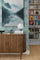 Elegant living room with a fluted wood sideboard, sculptural white lamp, and pastel blue geometric backdrop highlighting a misty lake landscape wall art with boats for a peaceful, refined vibe
