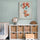 Pastel green nursery with large flying fox wall art, white cabinet with wicker baskets, globe and crib, soft natural decor