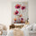 Dans cette chambre à la décoration minimaliste et naturelle, un grand tableau floral capte l’attention avec ses couleurs éclatantes et son style artistique audacieux. Le contraste entre les teintes chaudes des fleurs et la palette de couleurs neutres de la chambre crée une ambiance harmonieuse et apaisante. Les textures naturelles du mobilier en bois et des textiles renforcent l’élégance