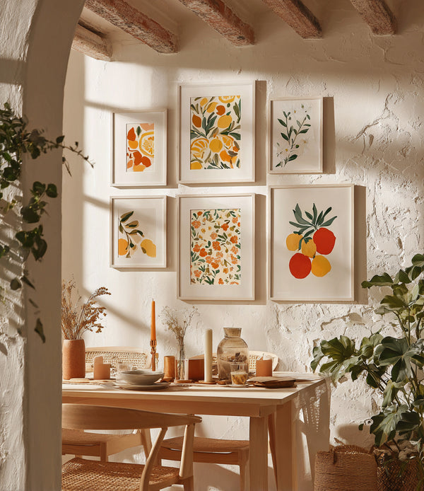 Mur de cuisine décoré avec des cadres illustrant des fruits et feuillages colorés, dans une ambiance méditerranéenne chaleureuse. Une table en bois clair est dressée sous une lumière naturelle, entourée de chaises en rotin et de bougies, créant une atmosphère douce et conviviale.