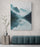 Large canvas of a misty mountain landscape with rowboats, hung on a light gray textured wall above a teal velvet tufted bench and raw wood side table for minimalist contemporary decor