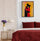 Cozy minimalist bedroom with abstract embracing couple wall art in warm orange, red, and yellow, red bedding, modern nightstand, white table lamp, purple flowers, and white walls