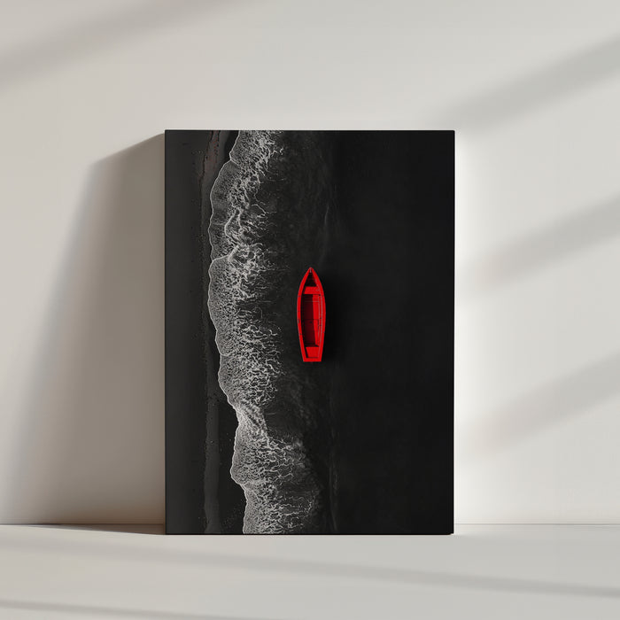 Vue aérienne d’une barque rouge flottant sur une mer noire, près d’une plage au sable sombre, avec des vagues blanches créant un contraste saisissant.
