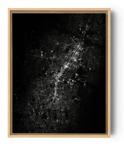Das Schwarz-Weiß-Bild zeigt eine nächtliche Luftansicht beleuchteter Straßen, die sich durch das dichte städtische Gewebe einer Stadt schlängeln