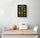 Styled kitchen scene: black framed chalkboard pasta poster centered on a white wall above a wooden dining table with two white chairs; white metal bread basket and a melon on the table