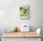 Small kitchen wall decor on a white wall: green grapes with leaves and orange slices; soothing palette, wood table, white chairs, melon and bread basket