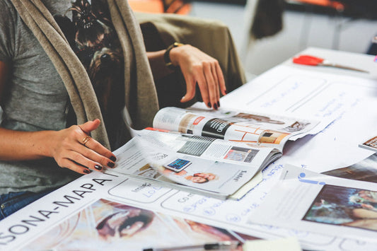 a person flipping through magazines on a table, highlighting illustrated pages with images of design, decor, or advertising