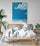 Primary bedroom decor with a large rattan bed, white bedding, wicker basket, wooden nightstand, large tropical plant, minimalist ocean print