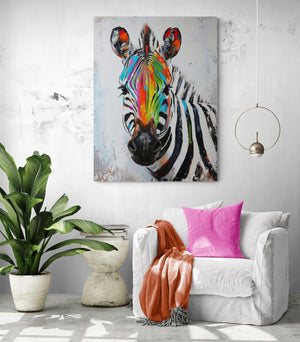 A colorful zebra painting is highlighted in a tropical living room, with a large white sofa, pink and salmon cushions, and a large green plant.