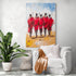 African-inspired wall art featuring five Maasai warriors walking away, showcased in a minimalist living room with a white chair, camel throw, and tropical plant.
