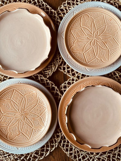 Assiettes en céramique artisanale posées sur des sets de table en fibre naturelle. Deux assiettes gravées de motifs floraux berbères et deux assiettes lisses vernissées en terre cuite, alliant simplicité et savoir-faire marocain traditionnel.
