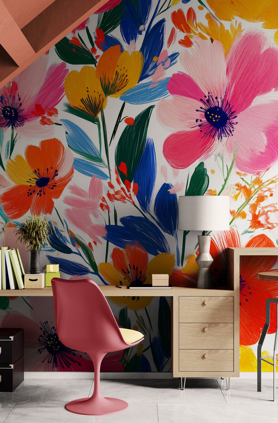 Un espace de travail lumineux agrémenté d’un papier peint floral aux couleurs vives. Le bureau en bois clair, la chaise rose et les éléments de décoration minimalistes créent un contraste harmonieux et un intérieur pétillant.