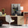 Light wood desk against a terracotta wall with a white chair and yellow cushion; deer-in-suit art print on the cabinet adds a quirky touch; modern lamp, stationery, and greenery complete the home office decor