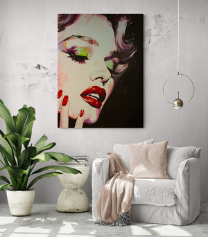Large Marilyn Monroe artwork, bright living room, comfortable chair with pale pink cushion and throw, side table with books, large green plant, pendant light fixture.