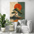 Japanese wall art depicting a lone pine on a rock facing a big red sun, displayed in a modern living room with white chair, gray cushion, decorative throw, green tropical plant, and small concrete design table.