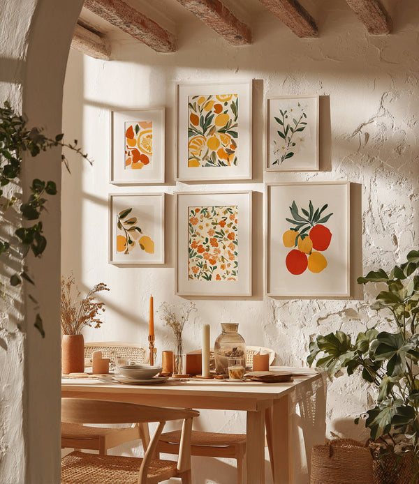 Kitchen wall decorated with frames illustrating colorful fruits and foliage, in a warm Mediterranean vibe. A light wooden table is set under natural light, surrounded by rattan chairs and candles, creating a soft and welcoming atmosphere.