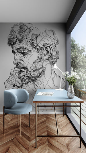 Modern office with artistic wall decor featuring a continuous line drawing of a bearded male face in contemporary sketch style. The space includes a pastel blue designer chair, a wooden desk with a light blue top, a minimalist white lamp, and a glass vase with white flowers, all bathed in natural light from a large window overlooking a garden