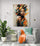 A bright room with green plants, creating a relaxing and inspiring space, with a painting of a black woman hanging on the wall above a white chair with a turquoise cushion and an orange throw.