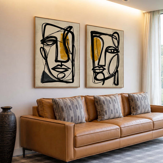 Salon moderne et lumineux avec canapé en cuir camel, grandes baies vitrées et deux tableaux abstraits visage noir et ocre accrochés au mur. Décoration intérieure élégante et contemporaine, idéale pour mettre en valeur des œuvres murales modernes dans un espace chaleureux et raffiné.