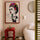 Decorative canvas featuring an artistic Frida Kahlo portrait with colorful flowers and a red frame, hanging in a modern beige bedroom with red side table and white lamp