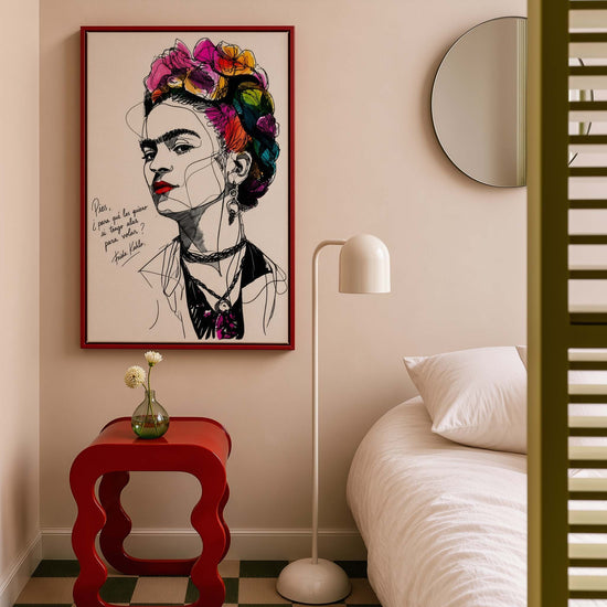 Decorative canvas featuring an artistic Frida Kahlo portrait with colorful flowers and a red frame, hanging in a modern beige bedroom with red side table and white lamp