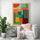 Large vibrant wall poster adds color to a cozy living room corner featuring a white chair and decorative green plants.