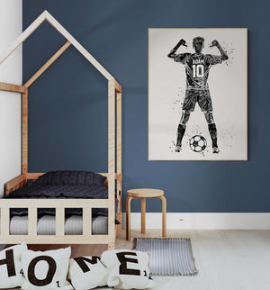 A modern and minimalist decorated child's room. On the wall, a large personalized poster depicts a soccer player seen from the back, with the name "Adam" and the number 10 on his jersey. The player raises his arms in victory. A simple wooden bed and cushions with the letters "HOME" add to the warm, sporty atmosphere of the room.