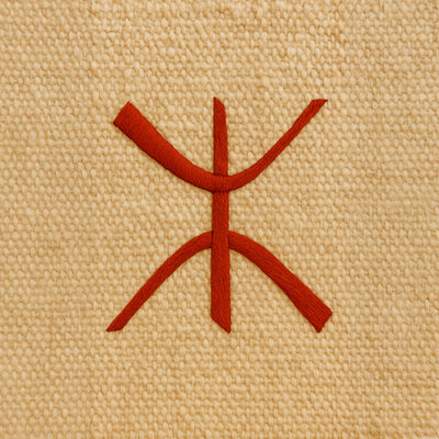 Symbole amazigh rouge tissé sur un fond en laine beige naturelle, représentant l’identité berbère et la culture ancestrale du peuple amazigh. Le motif, simple et graphique, incarne la fierté et la mémoire des traditions nord-africaines.