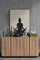 Black and white poster of a woman meditating, sitting in front of a calming landscape. Placed on a wooden sideboard and surrounded by decorative objects in neutral tones, it creates a relaxing and harmonious atmosphere. The raw concrete wall adds an industrial touch, contrasting with the serenity of the scene.