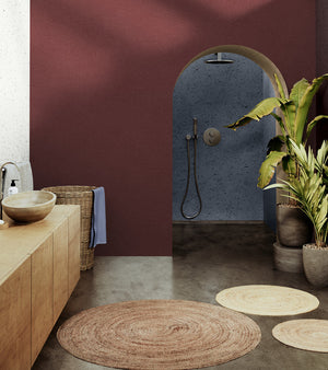 This natural and refined bathroom combines earthy tones with a deep burgundy wall and a built-in blue-gray shower. The concrete floor is warmed by natural fiber rugs. Tropical plants and light wood furniture complete the zen and organic atmosphere.