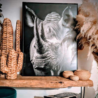 Avis client : tableau noir et blanc d’un rhinocéros en gros plan, posé sur une étagère en bois brut avec des éléments décoratifs naturels en osier, dans un intérieur au style bohème et chaleureux.