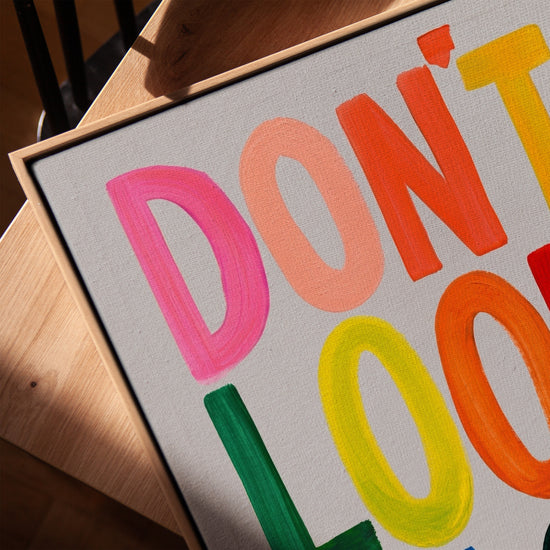 Don't Look Back canvas with multicolor lettering in light oak frame on table