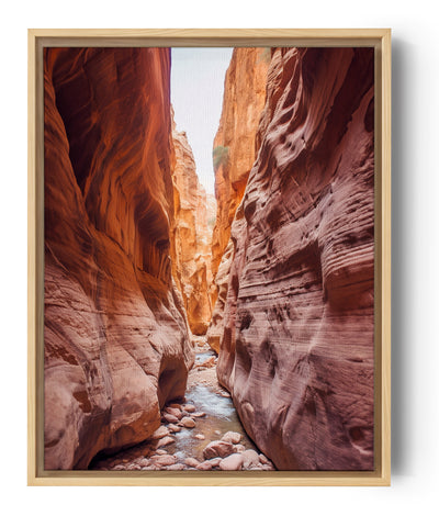 Das Foto zeigt einen schmalen Canyon mit rötlichen, durch Erosion geformten Wänden. Am Boden schlängelt sich ein mit Kieseln übersäter Bach und kontrastiert mit dem oben sichtbaren blauen Himmel.