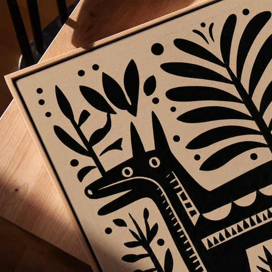 Cuadro infantil burro negro con motivos tribales y follaje beige, en mesa con marco de roble dorado