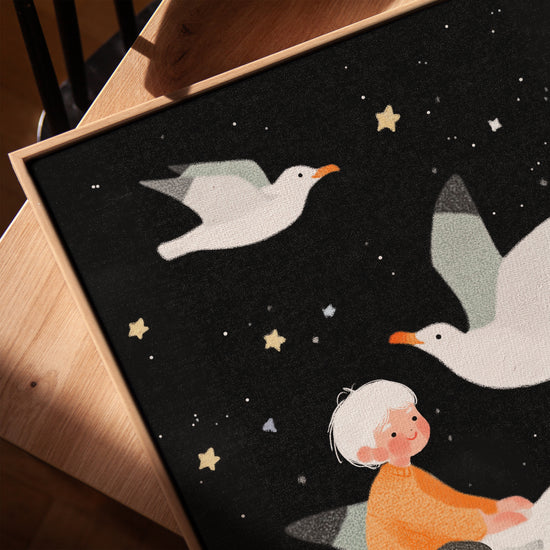 Nursery wall art of a child flying with birds and gold stars, golden oak frame on table
