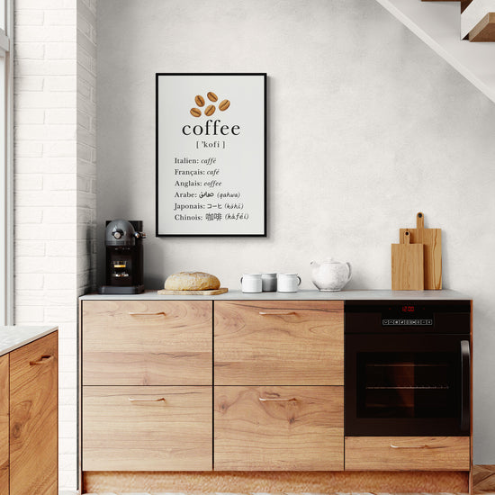 Affiche murale design sur le café en plusieurs langues, encadrée en noir et accrochée dans une cuisine scandinave avec machine à café et plan de travail en bois.