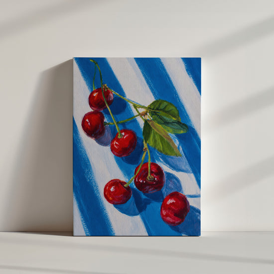 Minimalistisches, helles Leinwandbild: rote Kirschen am Zweig vor blau-weißem Streifenmuster
