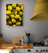 Un tableau de citrons jaunes et verts avec des feuilles vertes est suspendu sur un mur gris dans une cuisine équipée d'un plan de travail en bois et d'un capot de cuisinière jaune vif.