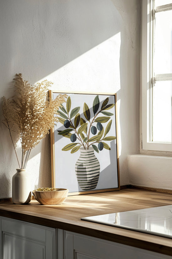 Art print depicting a striped vase filled with olive branches and black olives, sitting on a wooden countertop, bathed in natural light from a window. The scene exudes a soft, Mediterranean ambiance.