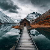 Photographie d’un chalet en bois isolé, au bord d’un lac paisible, entouré de montagnes enneigées. Le ponton en bois guide le regard vers la cabane, créant une atmosphère cosy et immersive. Parfait pour une décoration murale nature et apaisante.