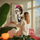 Decorative canvas of Frida Kahlo with colorful floral crown and red lips, hanging in a bright living room with pink chair and natural light, light wood American frame