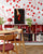 Reading nook with red shelves of books and bottles; wall art of a hand holding a red high heel on cherry-pattern wallpaper
