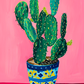 toile cactus en pot Botanique, fond rose, pot bleu et motifs jaune, style peinture.