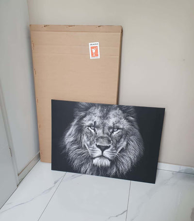 Customer review: black-and-white aluminum art print of a majestic lion, set on the floor in front of its packaging marked Fragile, on white marble-effect tile flooring.