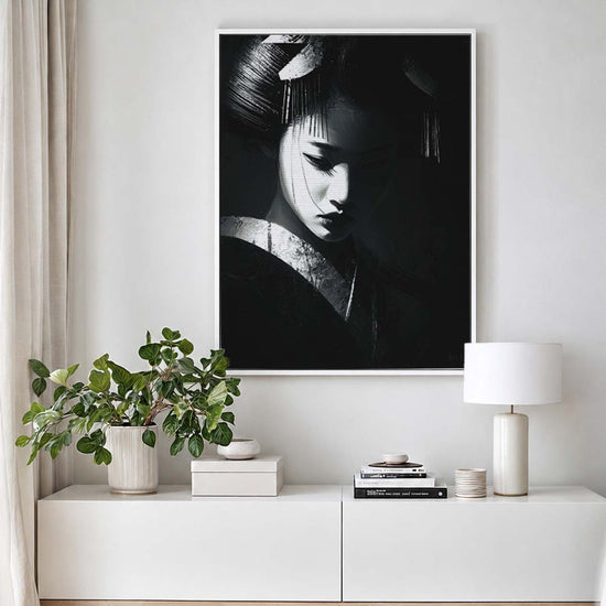 Tableau portrait noir et blanc représentant une geisha au regard baissé, accroché sur toile texturée dans un salon minimaliste lumineux avec meuble blanc, plante verte et décoration épurée