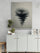 Monochrome black and white ink art of a water droplet and ripples, hung above a modern sideboard with potted plants, decorative books, and a light wood stool