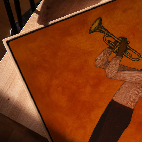Tableau musicien jazz trompette fond orange sur toile avec cadre chêne doré posé sur table